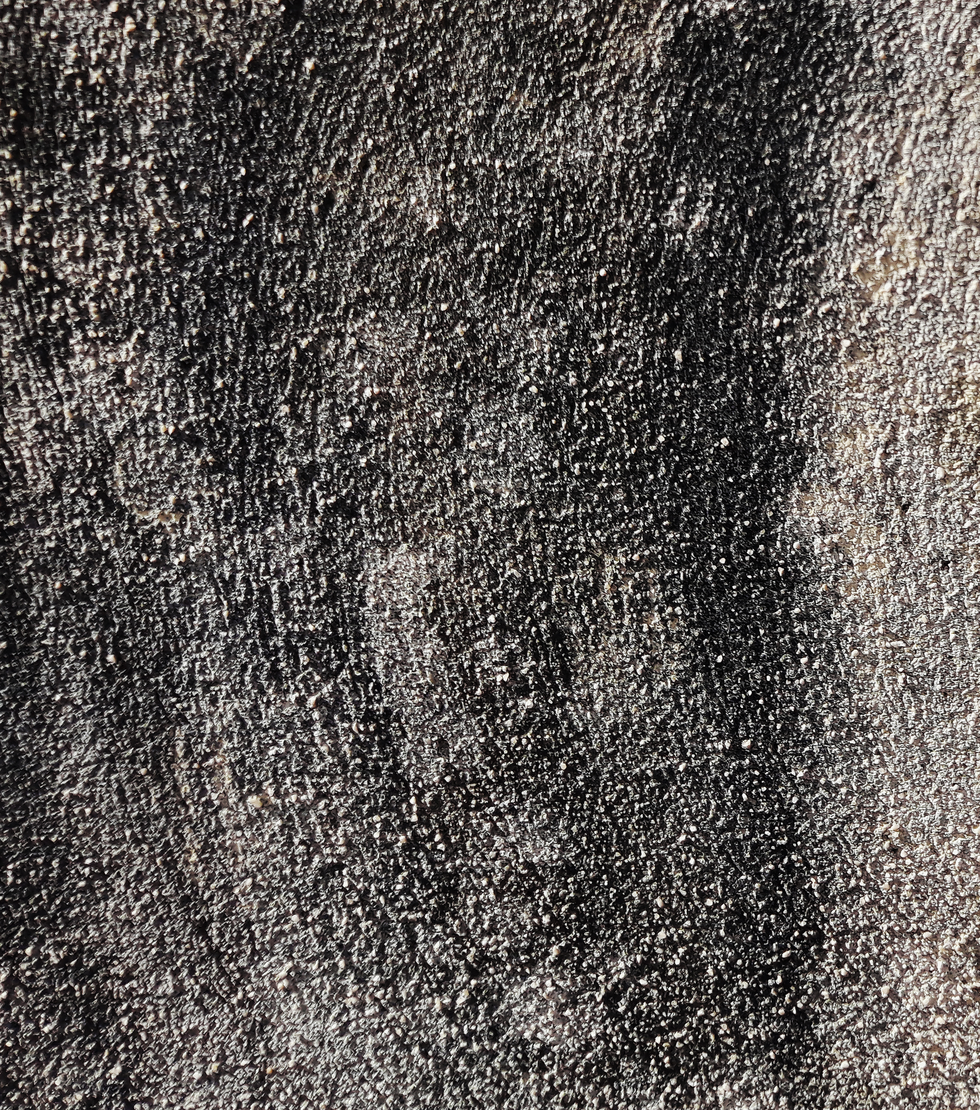 Gros plan sur une surface texturée, principalement gris foncé avec des mouchetures plus claires.