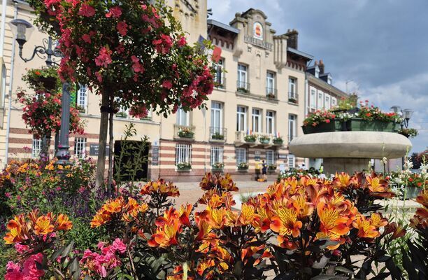 Forges-les-Eaux - Fleurs épanouies avec un bâtiment en arrière-plan. Hôtel de ville avec une tour d'horloge et une fontaine.