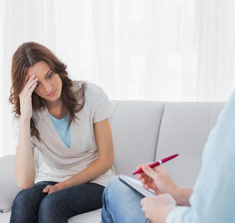 Una persona con expresión preocupada, con la mano en la frente, sentada frente a un profesional que toma notas.
