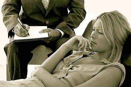 Una persona s'estira amb una expressió pensativa mentre un professional pren notes en una sessió de teràpia en tons sèpia.