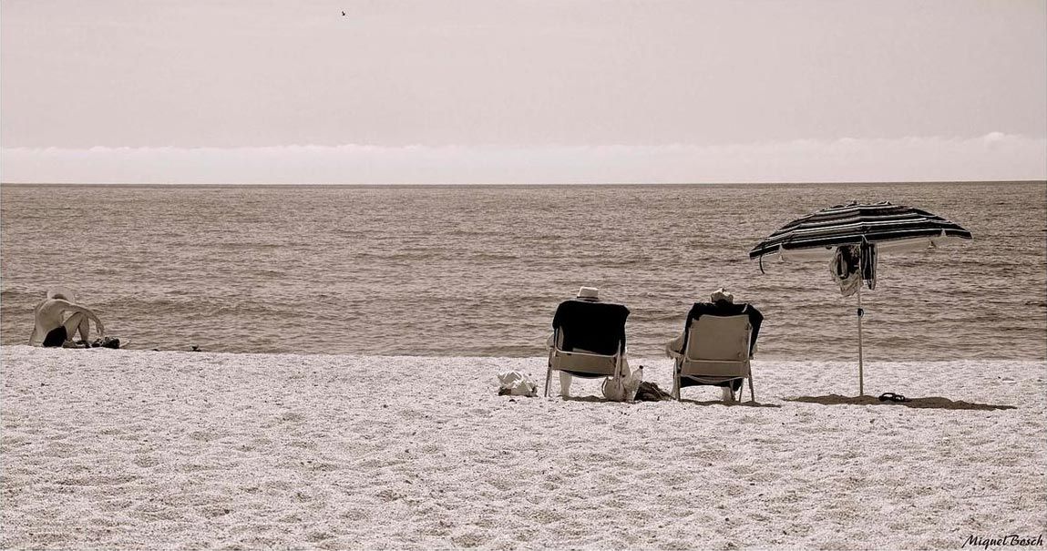 Dos tumbonas y una sombrilla de playa se encuentran en una orilla arenosa frente al océano tranquilo iluminado por el horizonte.