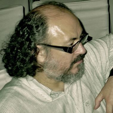Un profesional toma notas en un portapapeles mientras una persona yace en un sofá al fondo, gesticulando durante una sesión de terapia.