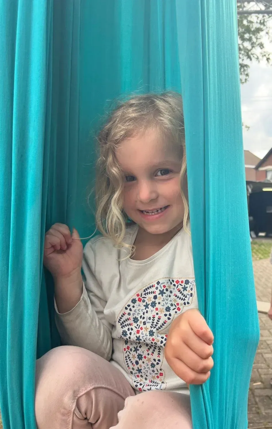 Un niño se asoma entre las cortinas turquesas con una sonrisa tímida en una puerta.