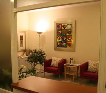Una sala de espera con sillas rojas y un cuadro en la pared.