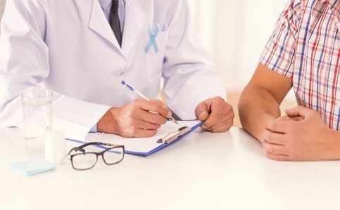 Un médico está escribiendo en un portapapeles mientras habla con un paciente.
