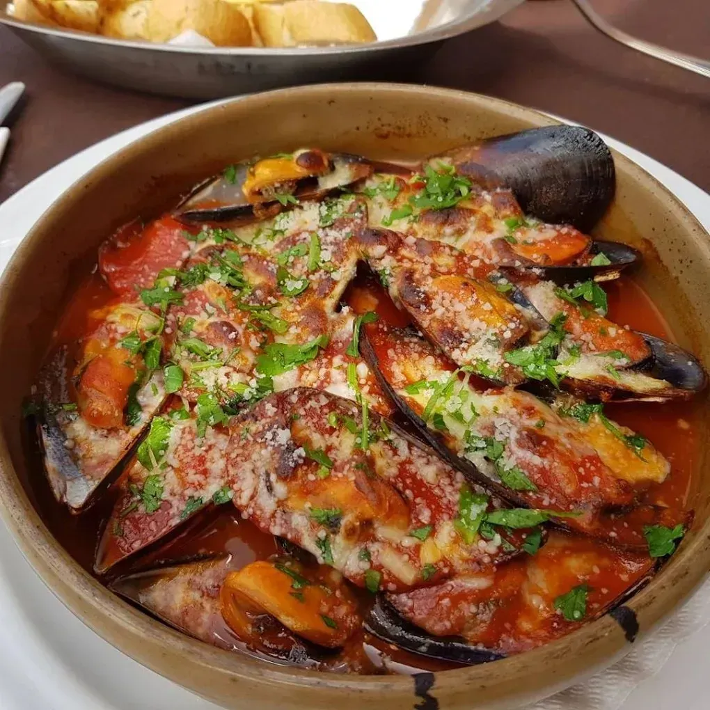 Mejillones al horno en salsa roja picante, adornados con hierbas, servidos en un plato redondo sobre una mesa.