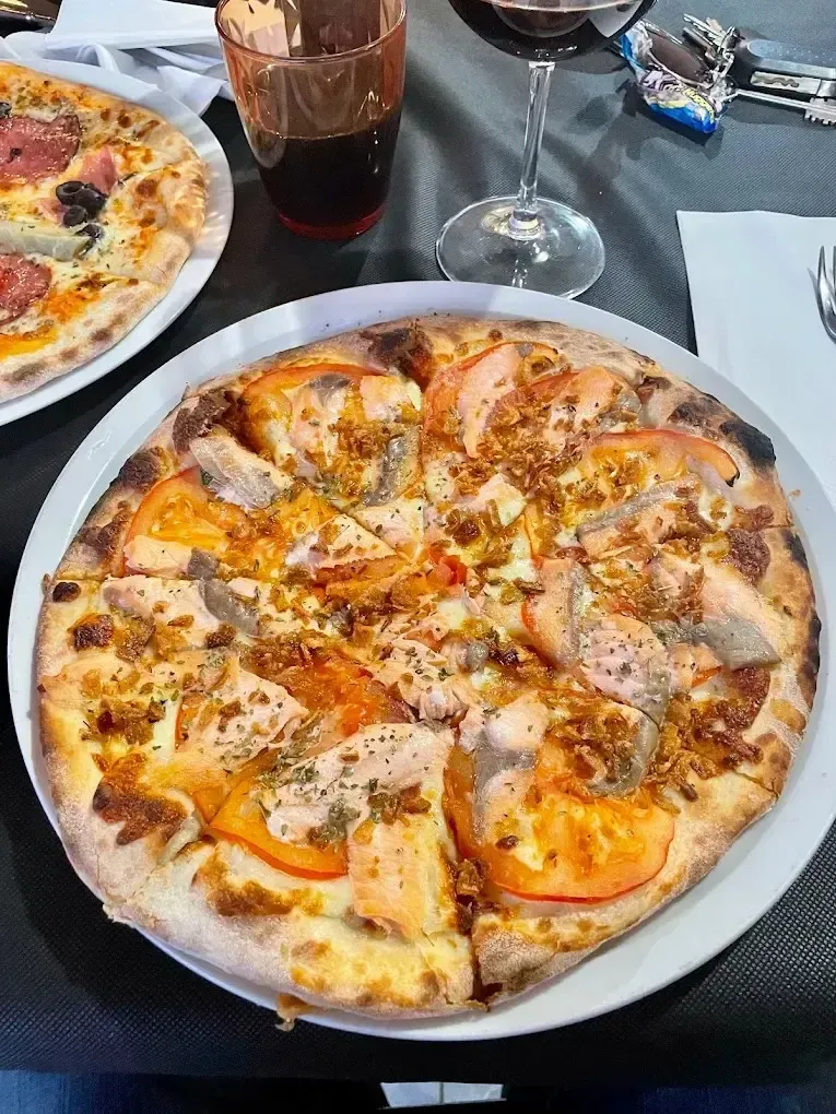 Dos pizzas sobre una mesa de restaurante con bebidas y vasos cerca.