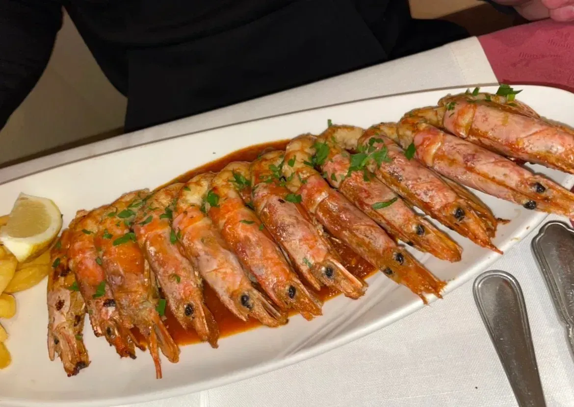 Plato de gambas a la parrilla con hierbas y rodajas de limón sobre una bandeja blanca con pinzas.