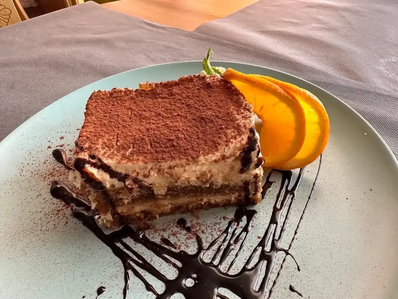Postre de tiramisú en un plato con rodajas de naranja y sirope de chocolate.