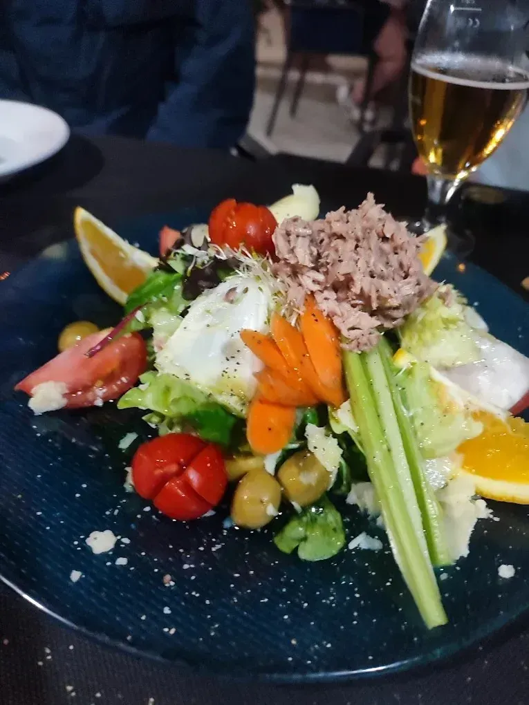 Ensalada con atún, tomates, verduras y una rodaja de limón, acompañada de una copa de vino blanco.