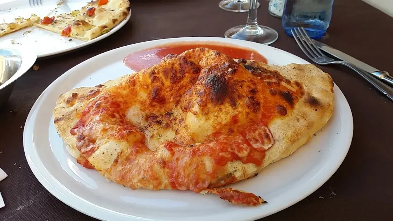 Pizza de queso en un plato blanco en la mesa de un restaurante, con una porción parcialmente comeda al fondo.