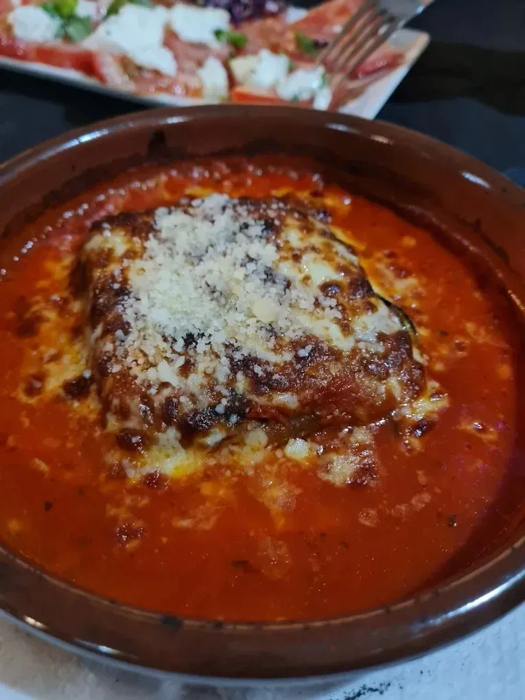 Pasta al horno con salsa marinara roja y queso fundido en un plato marrón.