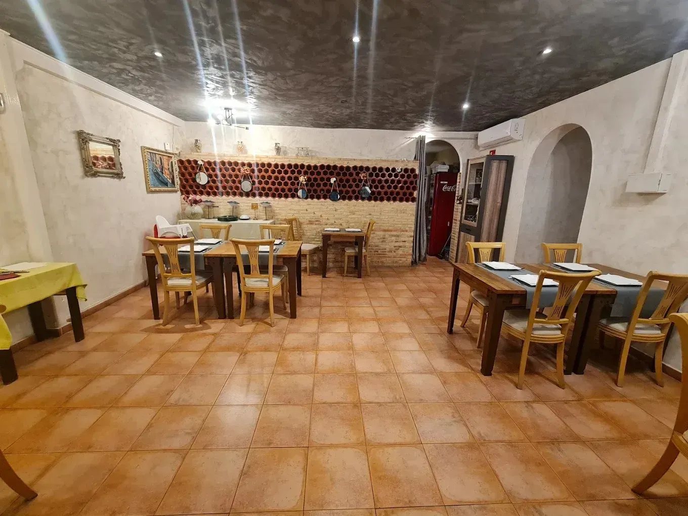Acogedor comedor rústico con mesas y sillas de madera, suelo de baldosas de terracota y puertas arqueadas.