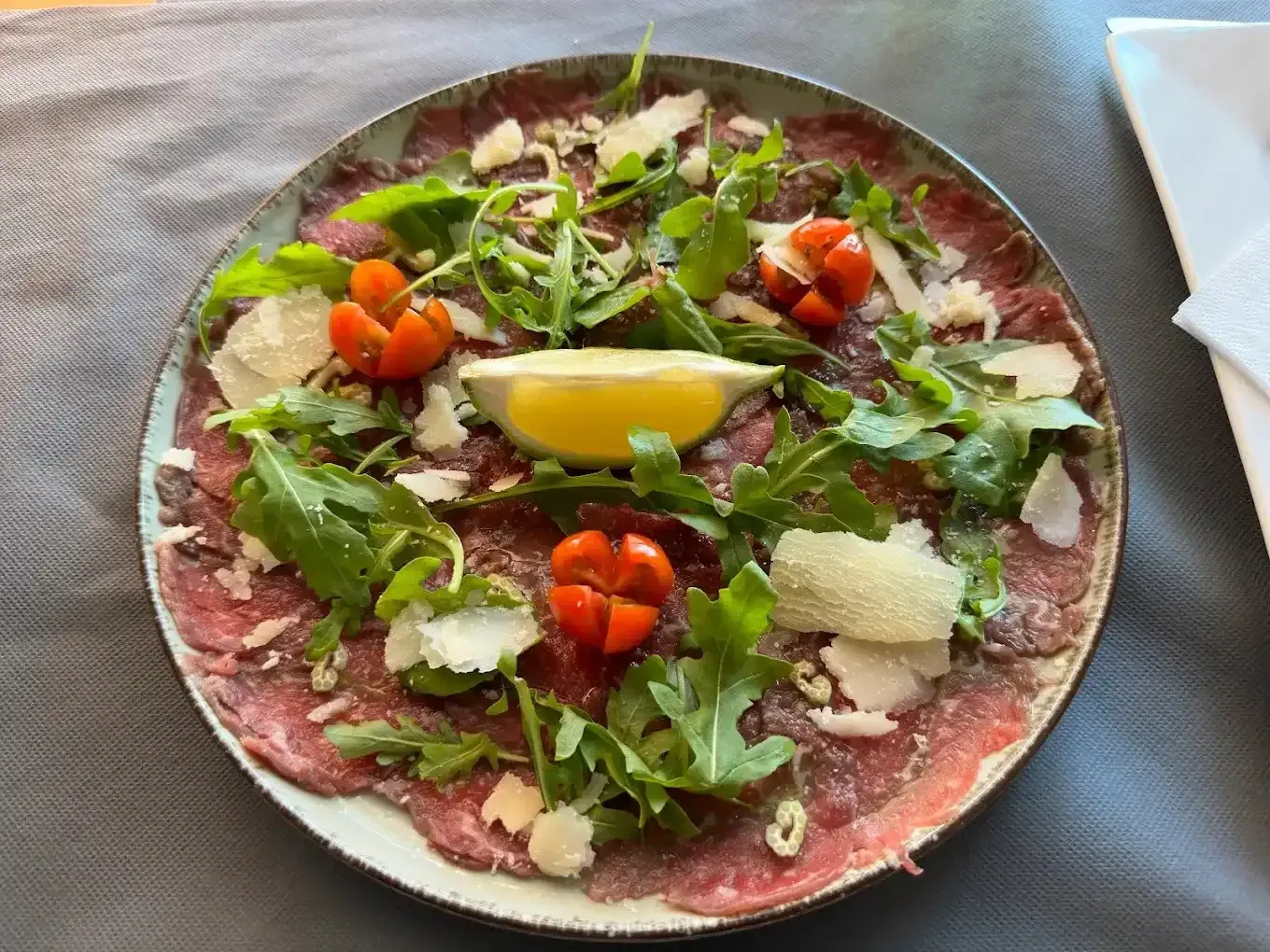 Vista aérea de una pizza cubierta con rúcula, tomates cherry, parmesano y una rodaja de limón.