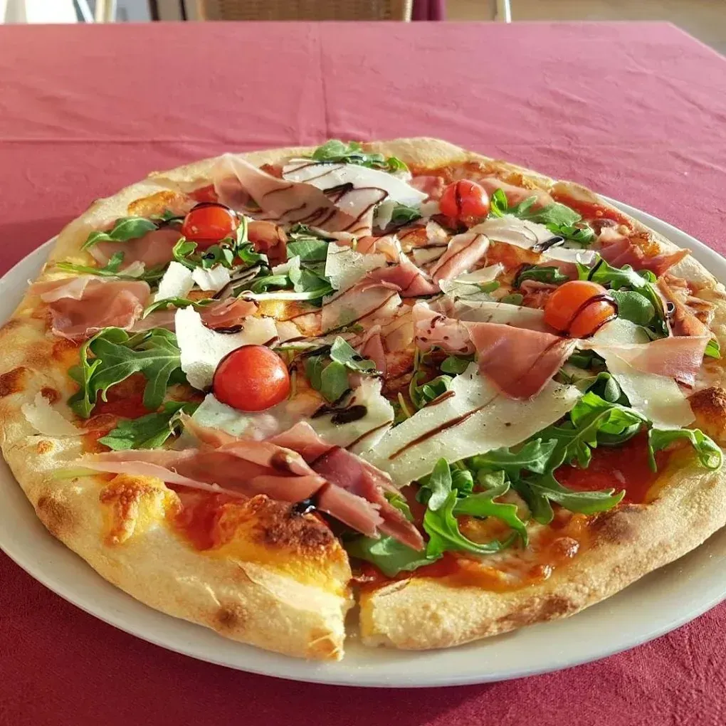 Pizza cubierta con rúcula, tomates cherry, jamón serrano y mozzarella en un plato blanco.