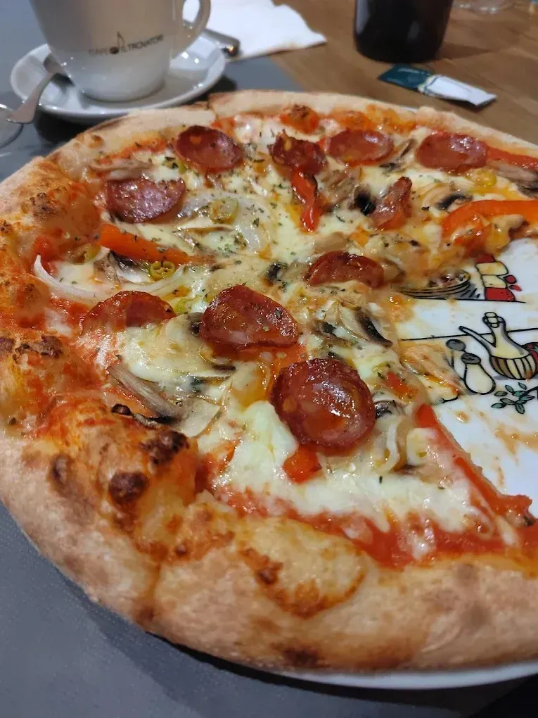 Pizza de pepperoni sobre una mesa con un vaso y una servilleta al fondo.