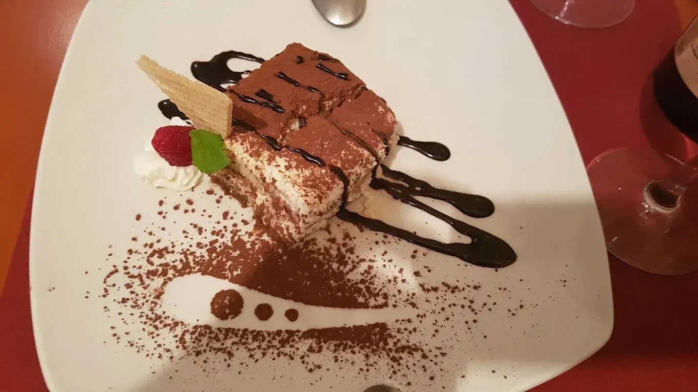Postre de chocolate en un plato blanco, rociado con salsa y espolvoreado con cacao