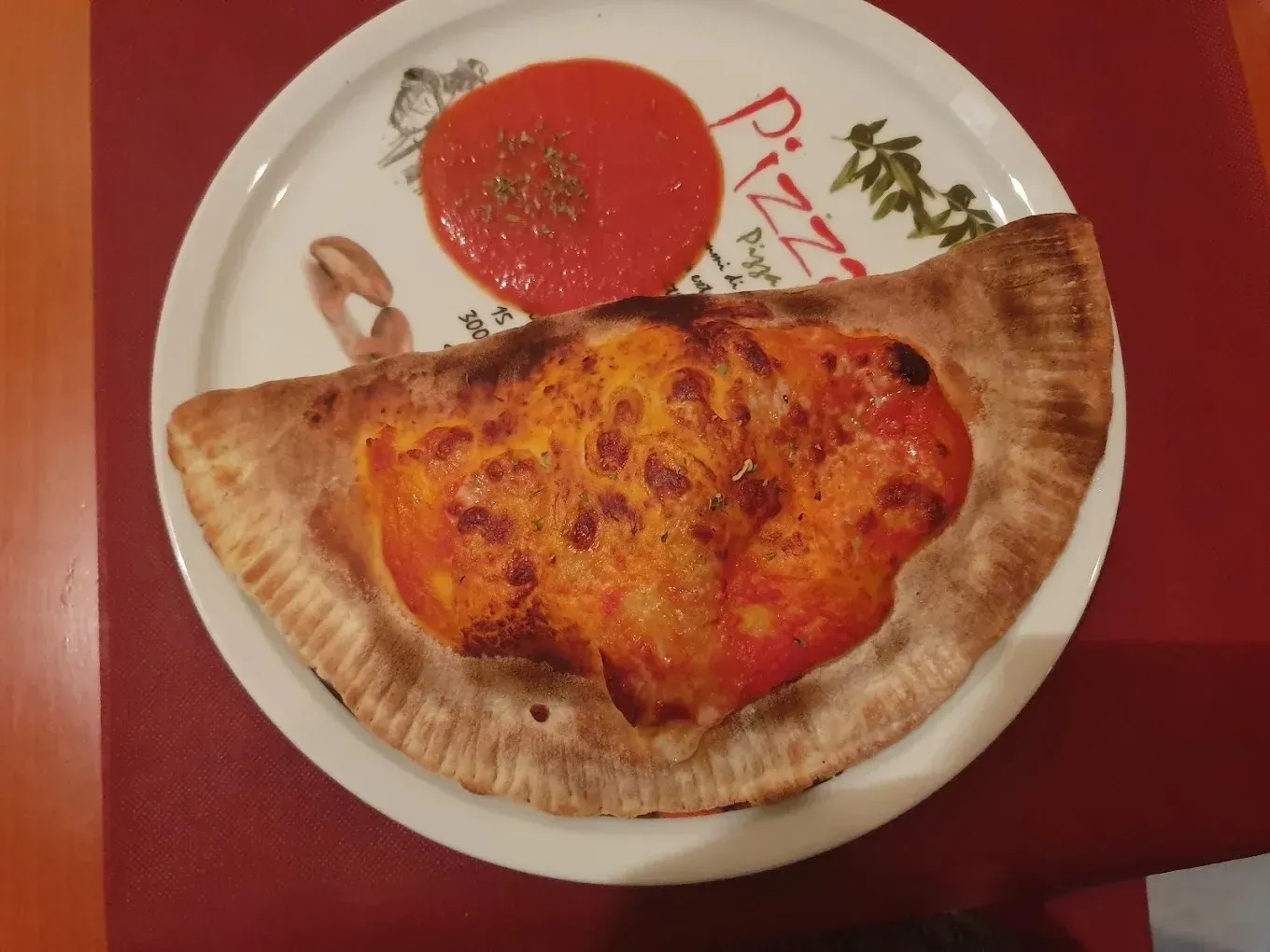 Pastelito horneado doblado con salsa de tomate en un plato blanco sobre un mantel rojo.