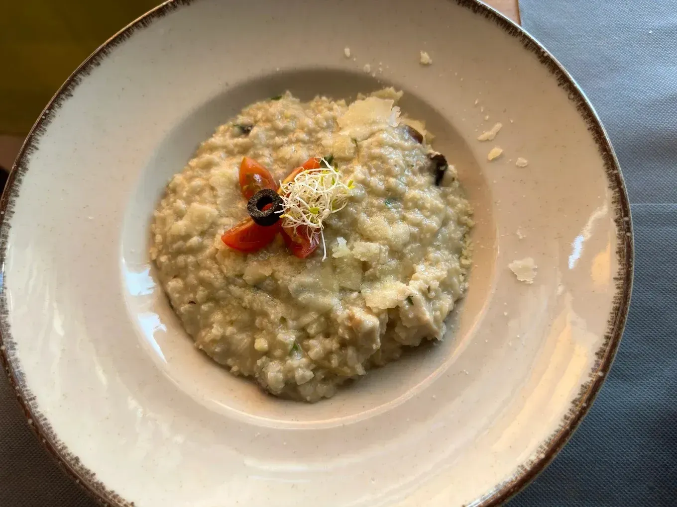 Un tazón de risotto cremoso cubierto con guarnición roja y queso rallado sobre una mesa.