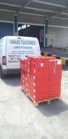 Una furgoneta blanca está estacionada al lado de un palé de cajas rojas.