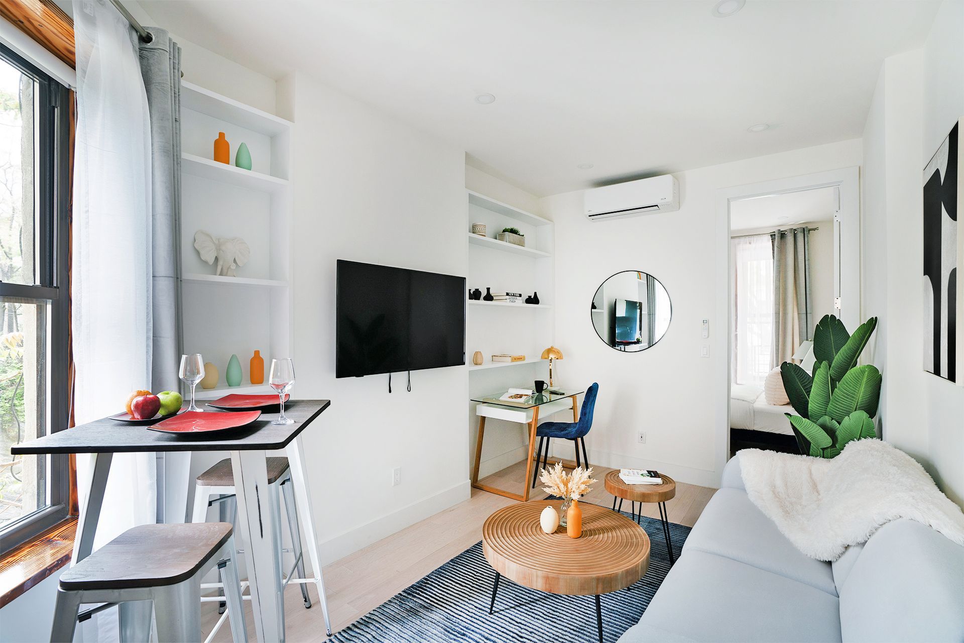 Modern one-bedroom apartment with a cozy seating area, wall-mounted TV, small dining table, and a desk area. The apartment is located in Midtown West and includes a washer and dryer.