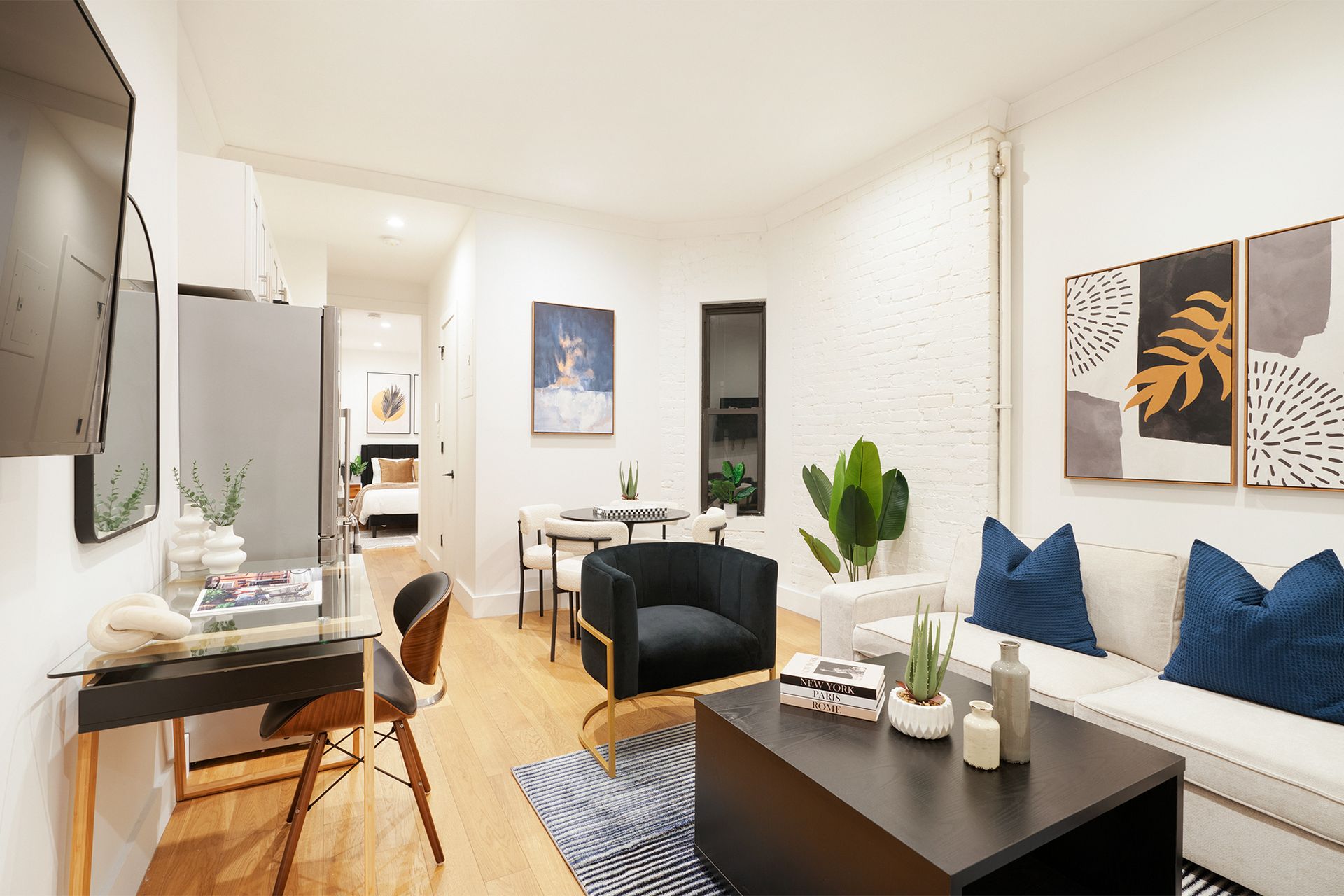 Contemporary two-bedroom apartment with a white sofa, black coffee table, round dining table with black chairs, wall-mounted TV, and abstract wall art. The apartment is located in the Upper East Side.