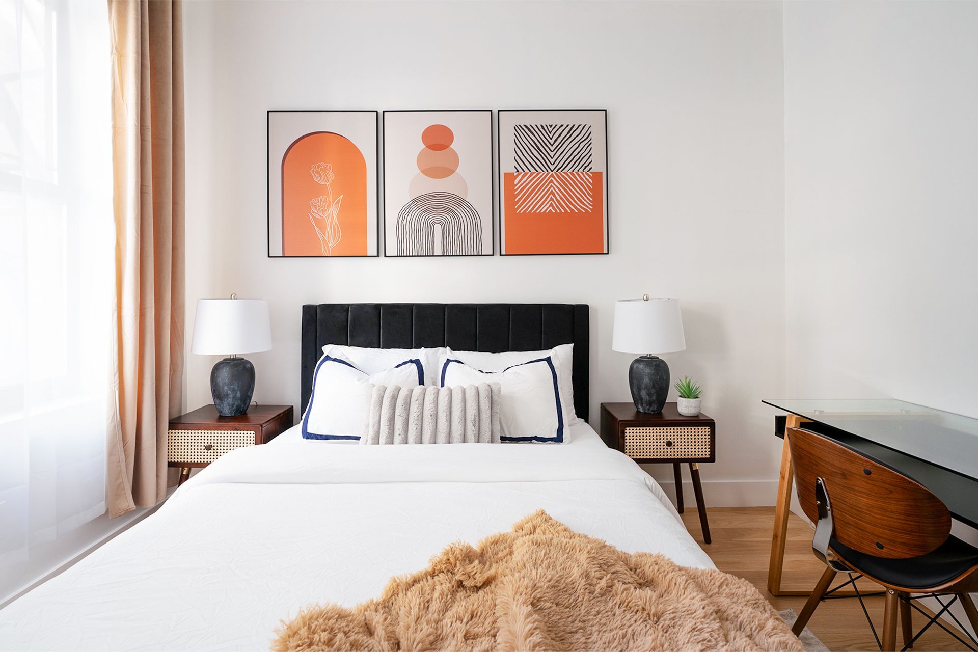 Modern two-bedroom apartment with white bed, black headboard, wall art, woodenightstands, and desk in the Upper East Side.