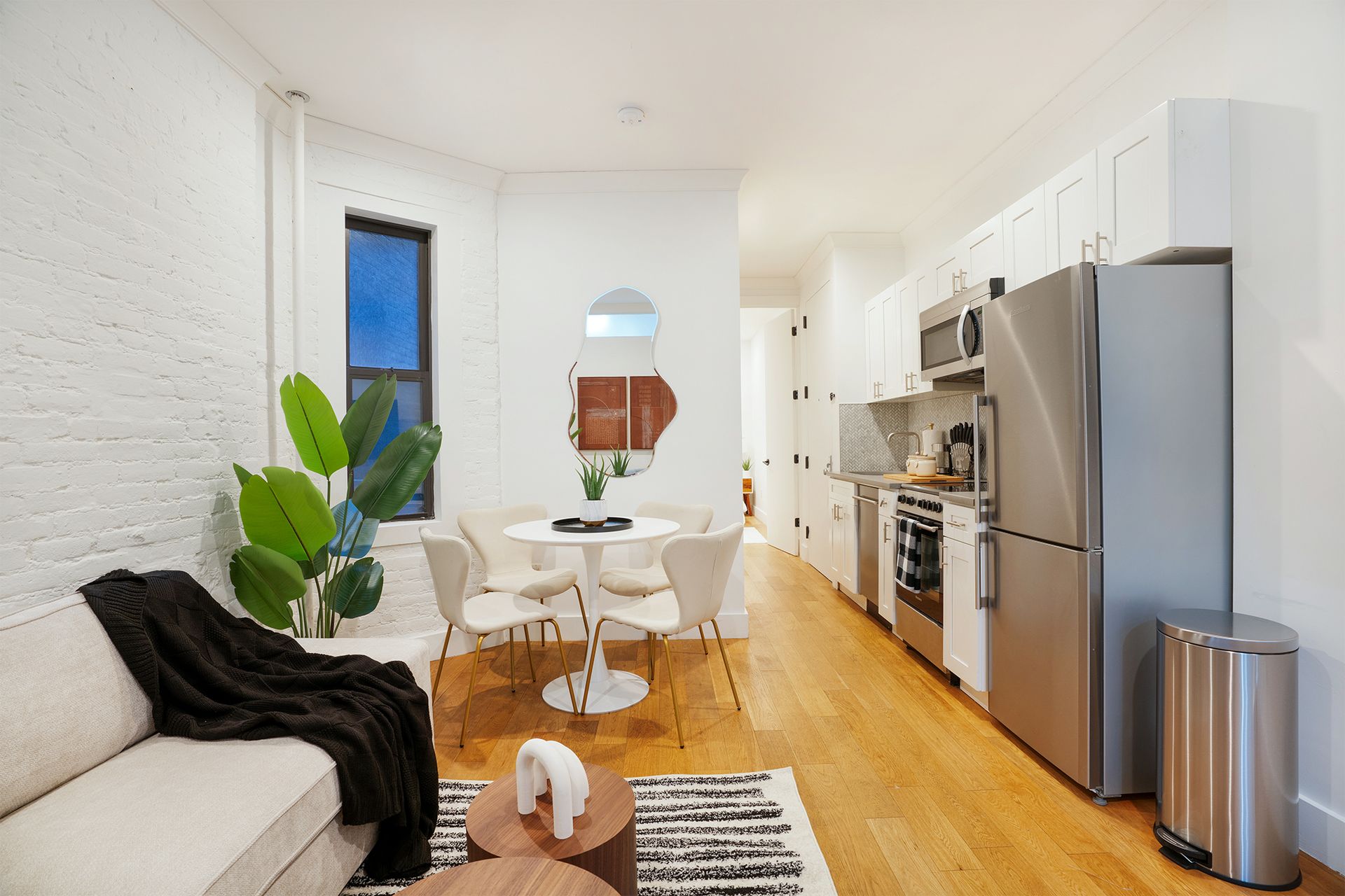 Two-bedroom apartment with sofa, coffee table, chairs, stainless steel appliances, and potted plant in the Upper East Side