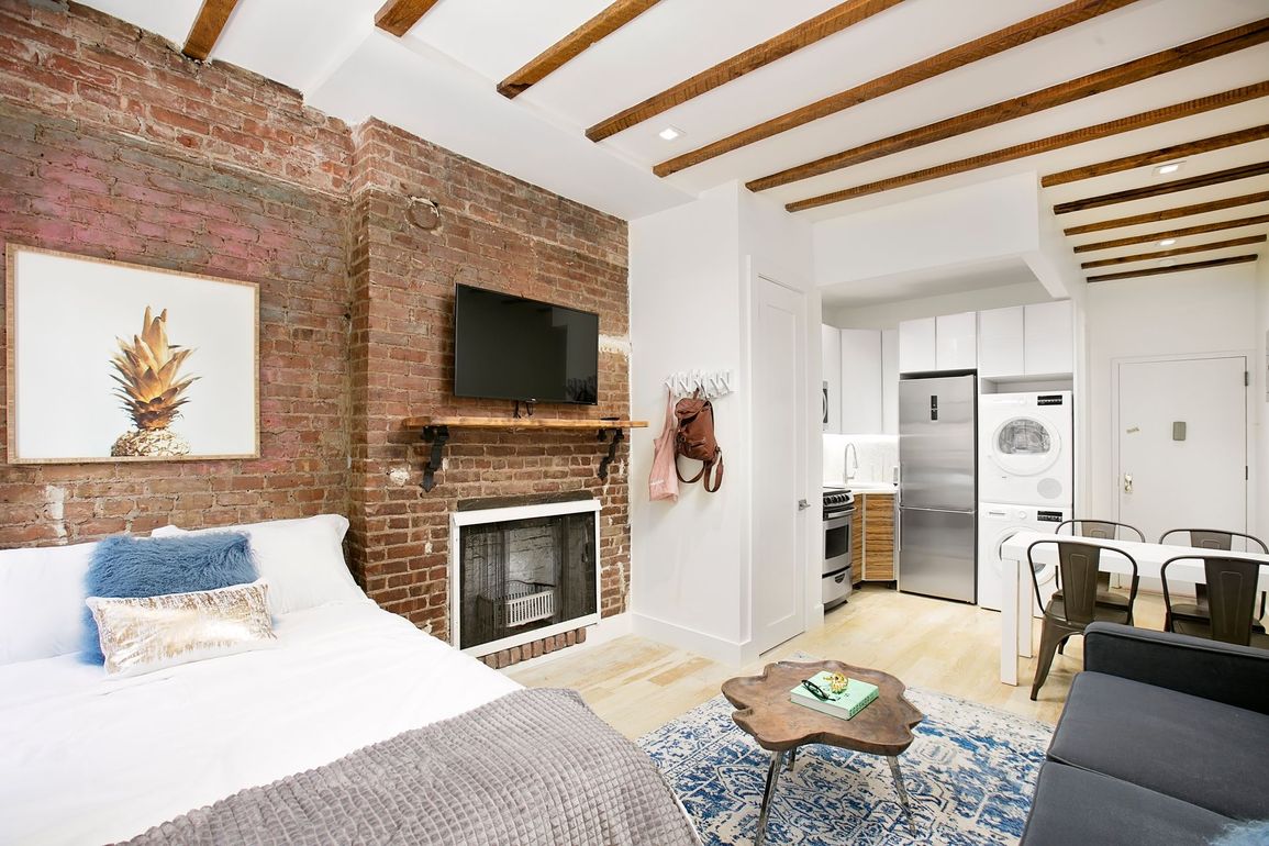 Small studio apartment with exposed brick, fireplace, and open kitchen.