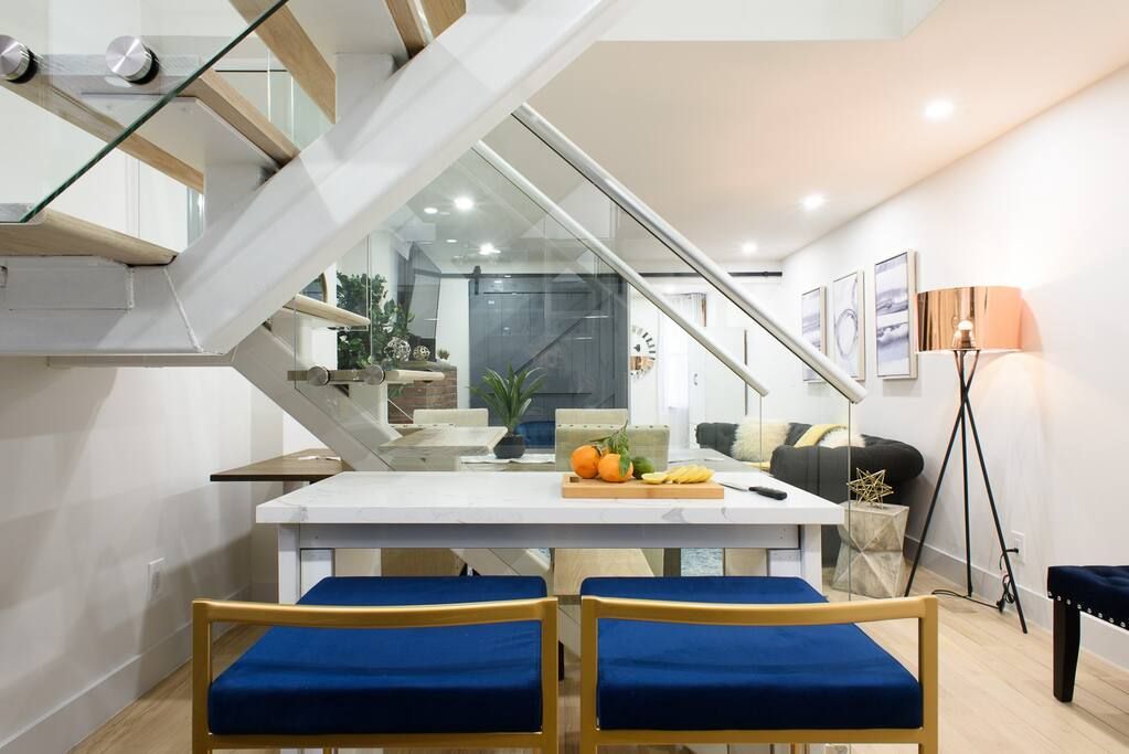 Three-bedroom apartment with white kitchen island,  glass staircase, sofa, and coffee table. It also has a washer/dryer.