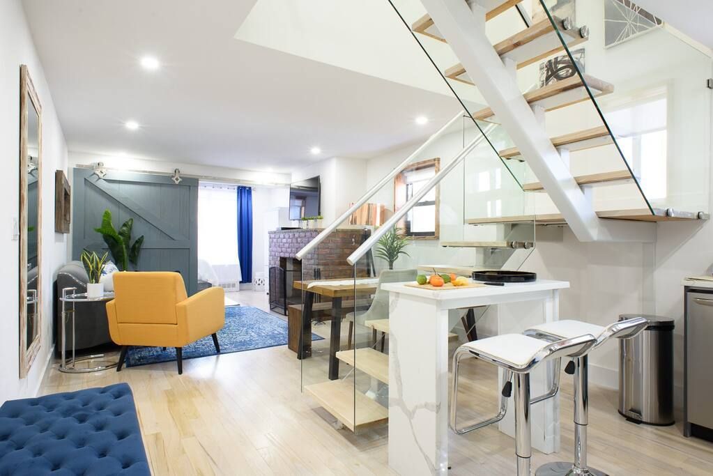 Spacious three-bedroom apartment with a modern kitchen, white countertops, glass staircase, yellow armchair, and blue rug. The apartment has a washer and dryer and an in-unit elevator.