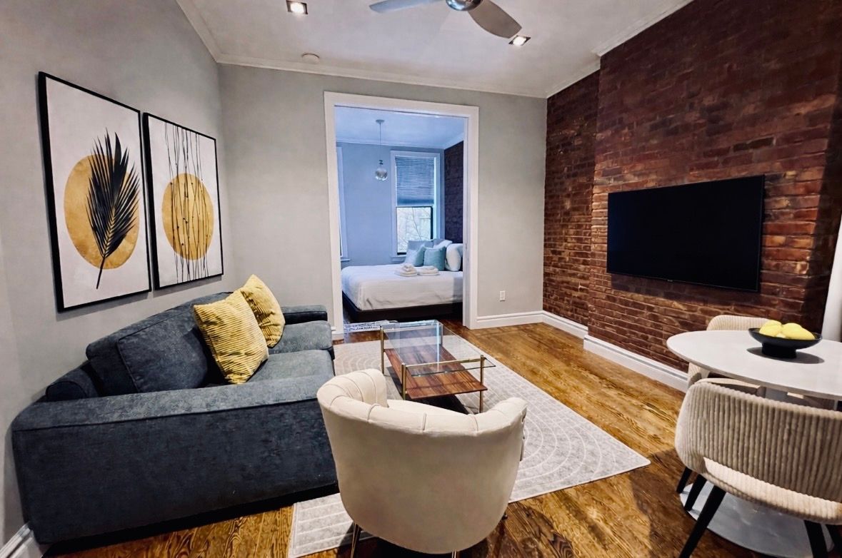 Bedroom with white walls, large bed, wood dresser, cloud mirror, and two windows with sheer curtains.