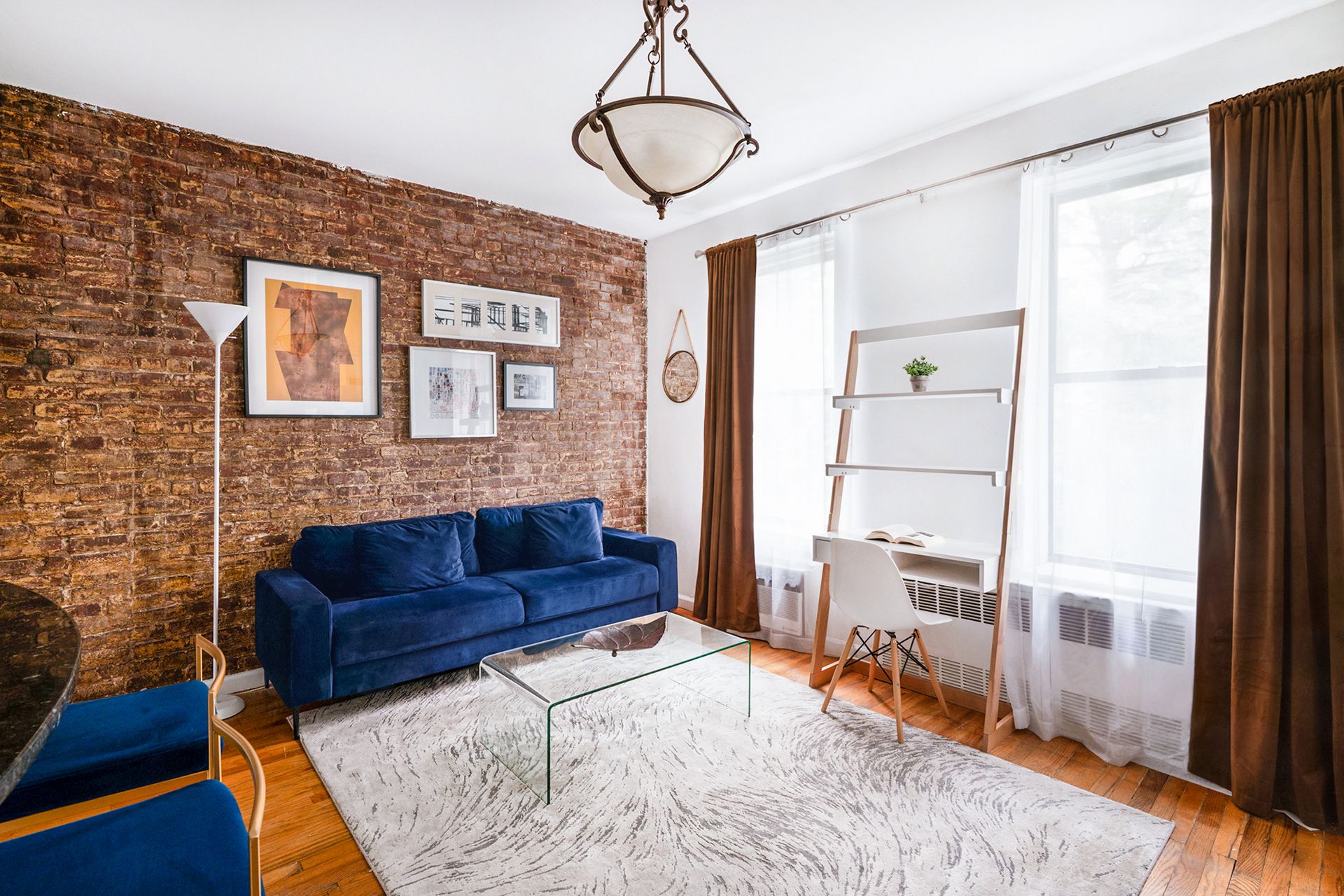 Cozy living room with brick wall, blue sofa, and work area by windows.