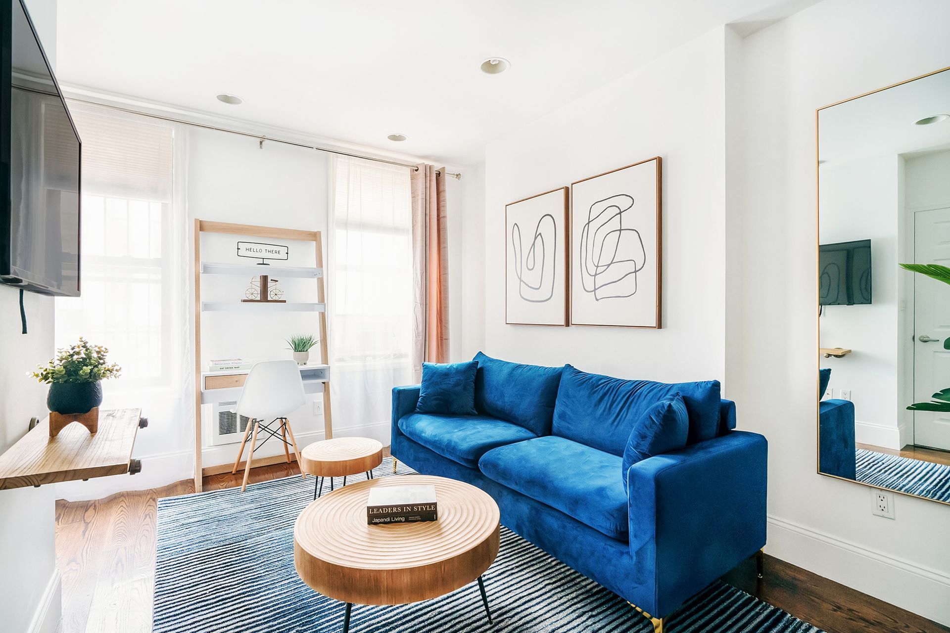 Stylish 1-bedroom apartment in the Lower East Side with a yellow sofa, blue area rug, minimalist wall art, blue curtains, a small workspace, and a cozy living area with a TV.