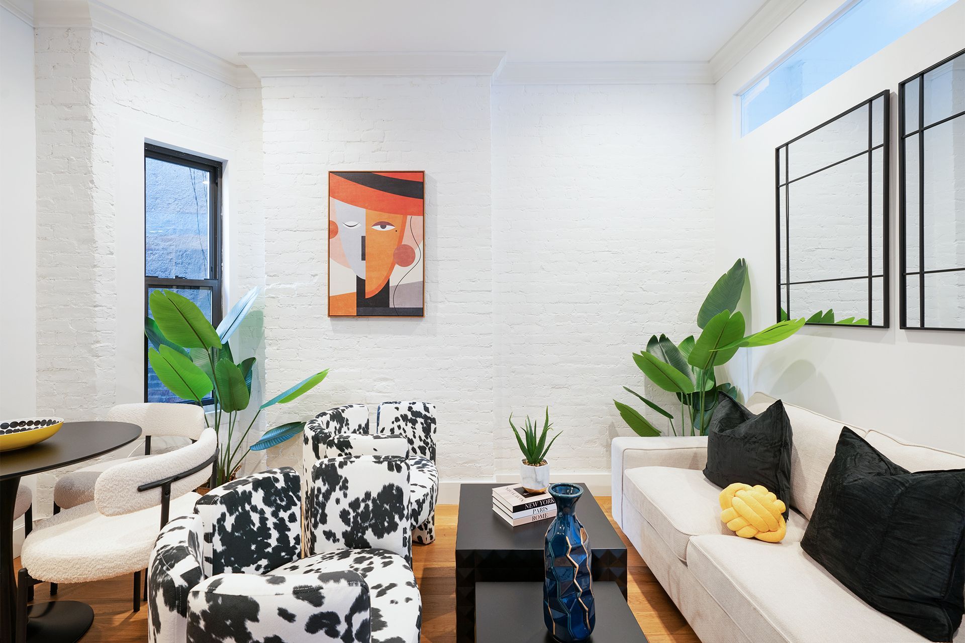 Contemporary two-bedroom apartment with a white sofa, black and white patterned armchairs, a colorful wall art, and a wooden coffee table. The apartment is located in the Upper East Side.