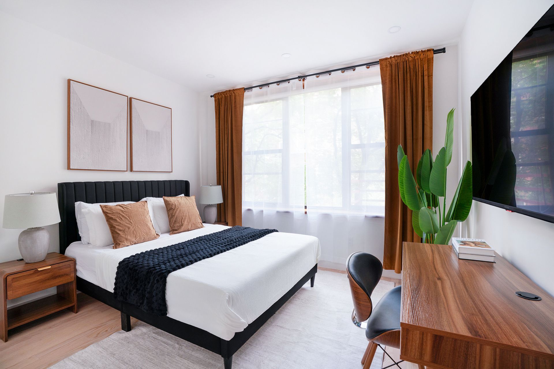 Bedroom with a bed, desk, and large TV. Neutral tones with orange and brown accents.