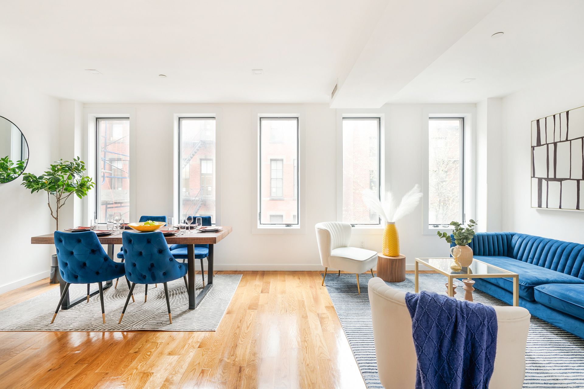 Spacious 3-bedroom duplex in Union Square with a private roof deck. Features a bright living area with blue chairs and a matching sofa, a dining table, and large windows allowing ample natural light.