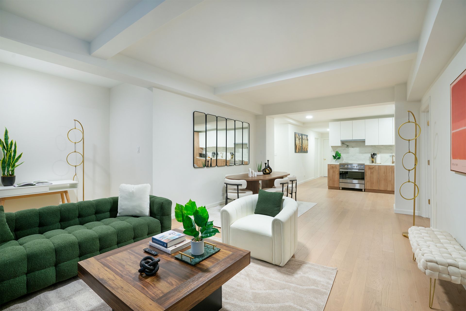Spacious four-bedroom apartment with a green tufted sofa, white armchair, wooden coffee table, dining area with a round table and chairs, and a modern kitchen with stainless steel appliances. The apartment features a large wall mirror and is located in the Upper East Side, with amenities including a 24-hour doorman and a gym.