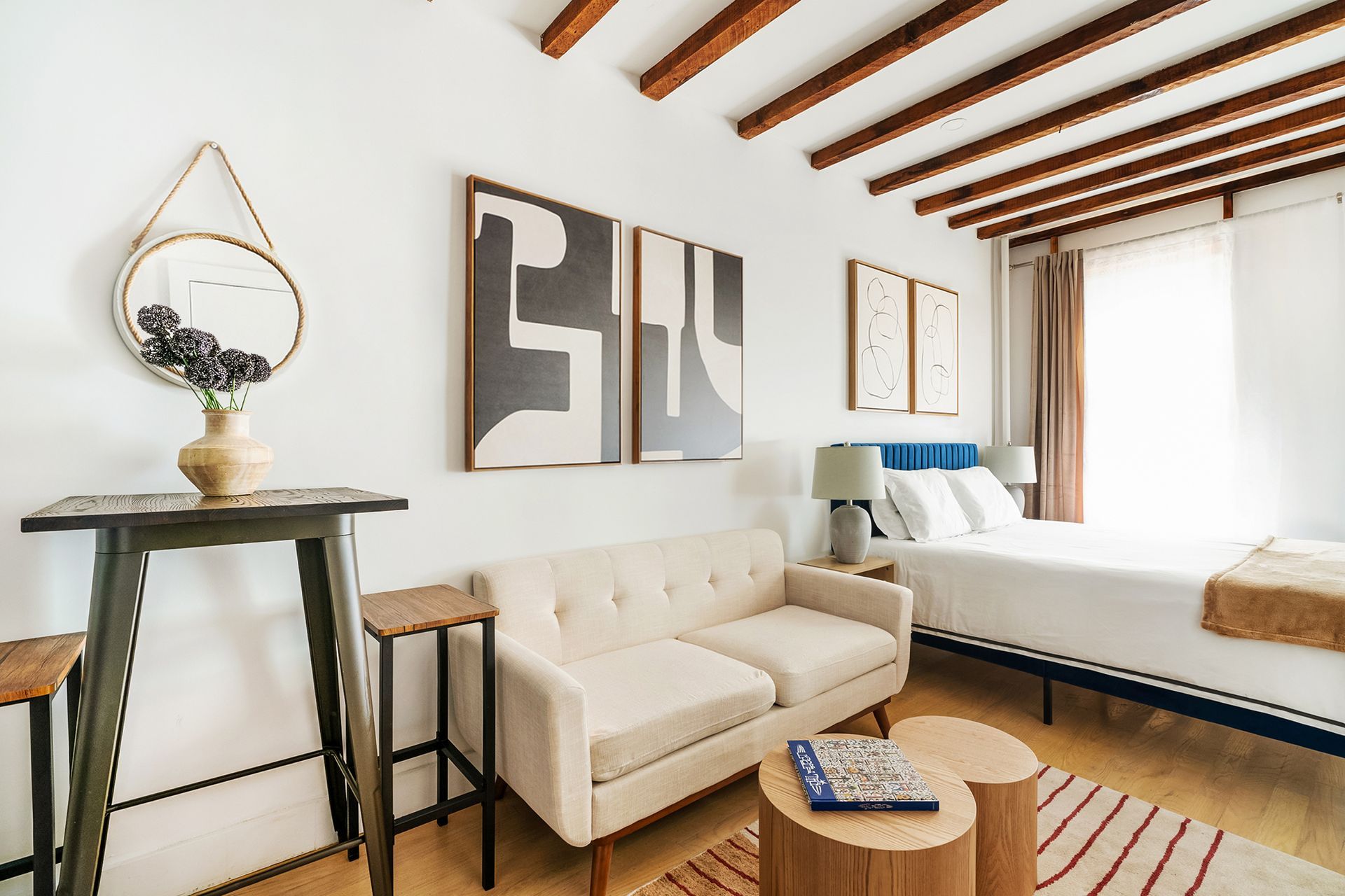 Studio apartment with yellow armchair, wooden beams, and a washer/dryer in the kitchen area. Located in Gramercy/Murray Hill.