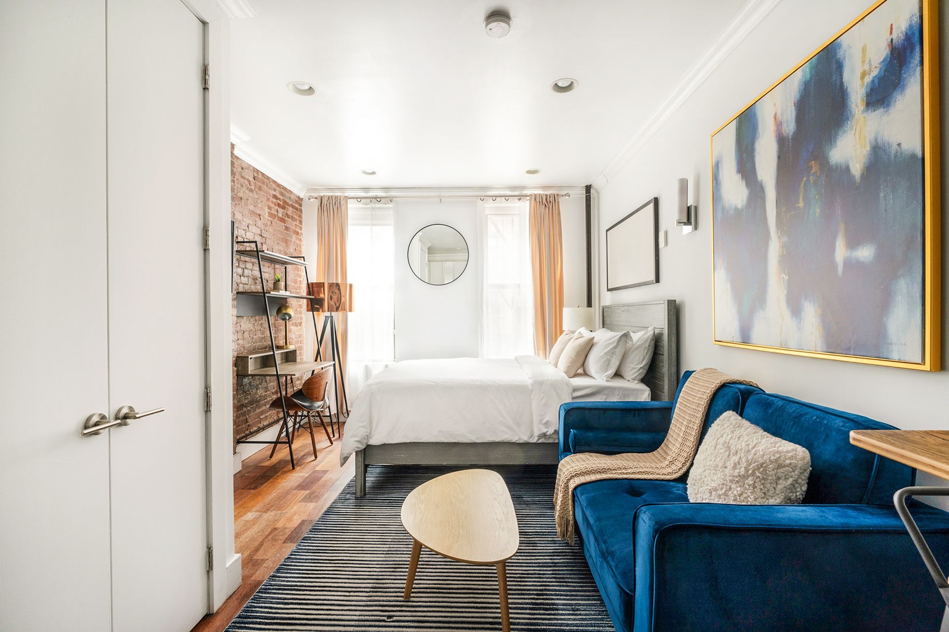 Modern studio apartment with large bed, grey curtains, orange chair, and a washer and dryer. Located in Gramercy/Murray Hill.