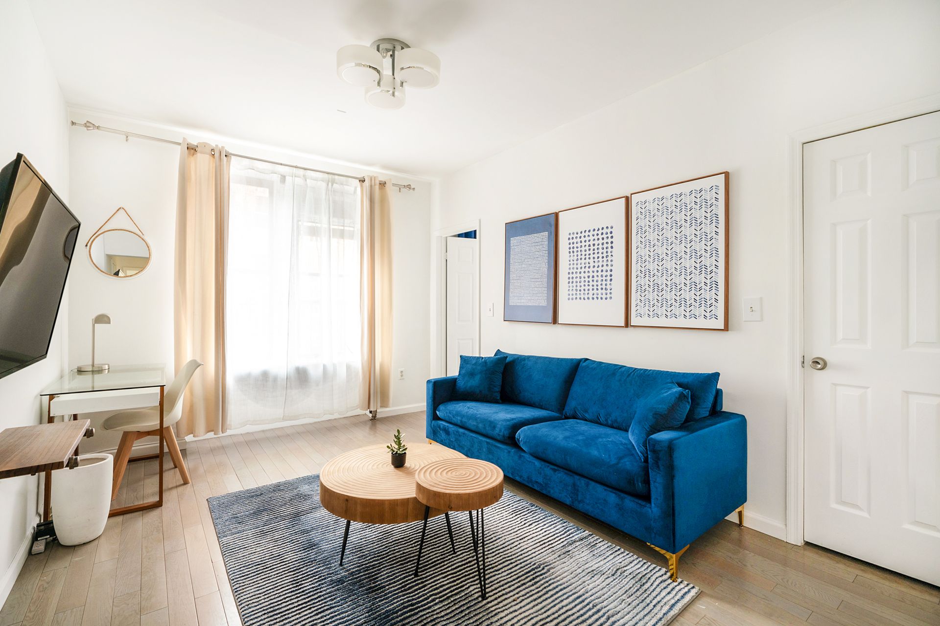 Bright two-bedroom apartment with a living room featuring a blue sofa, wooden coffee table, blue area rug, and a large window allowing ample natural light. Located in Midtown West.