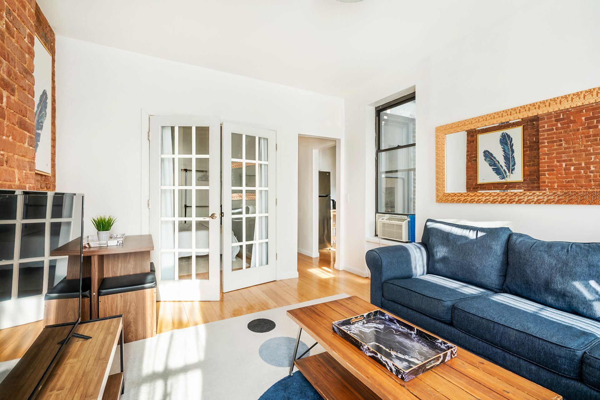 Charming two-bedroom apartment with a living room that includes a blue sofa, wooden coffee table, exposed brick wall, large mirror, and a work desk. Located in Midtown West.