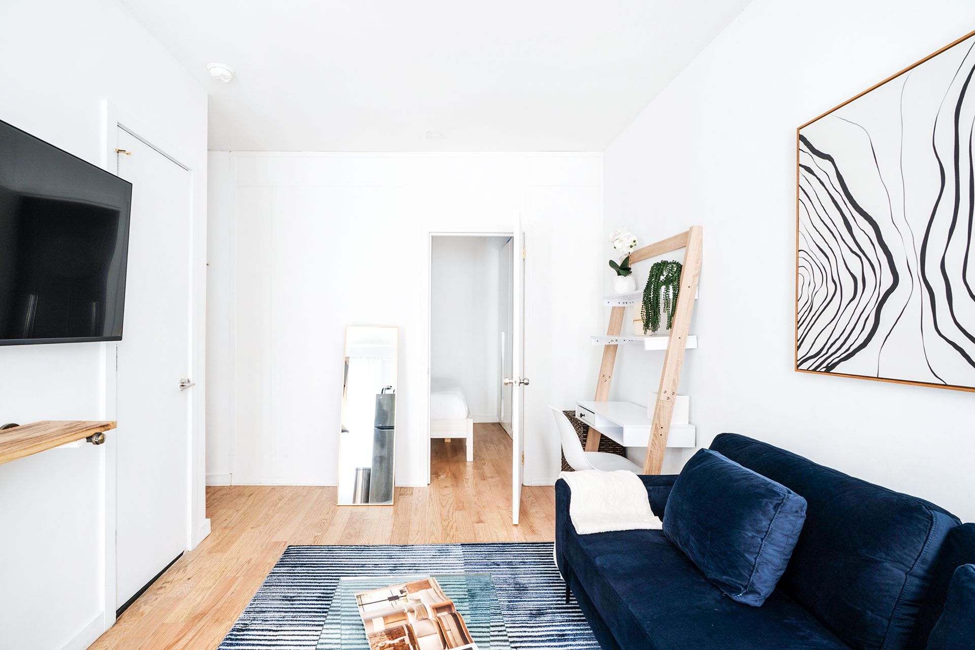 Charming 1-bedroom apartment in the Lower East Side with a stylish yellow sofa, white walls, wooden floor, decorative wall art, a small glass coffee table, and a cozy workspace.