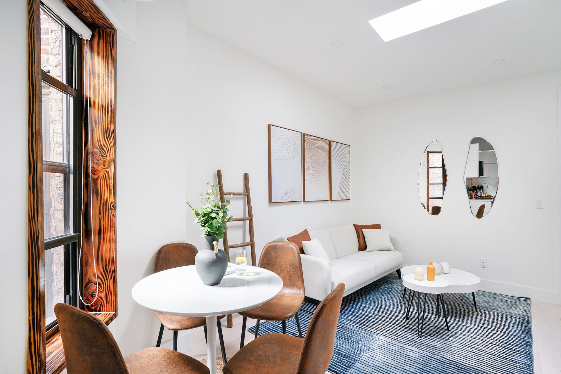 Cozy one-bedroom apartment featuring a seating area with a round dining table, modern decor, and large windows. The apartment includes a washer and dryer and is located in Midtown West.