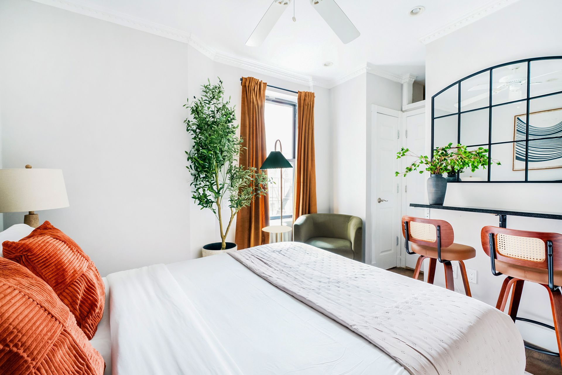 Bedroom with white walls, large bed, wood dresser, cloud mirror, and two windows with sheer curtains.