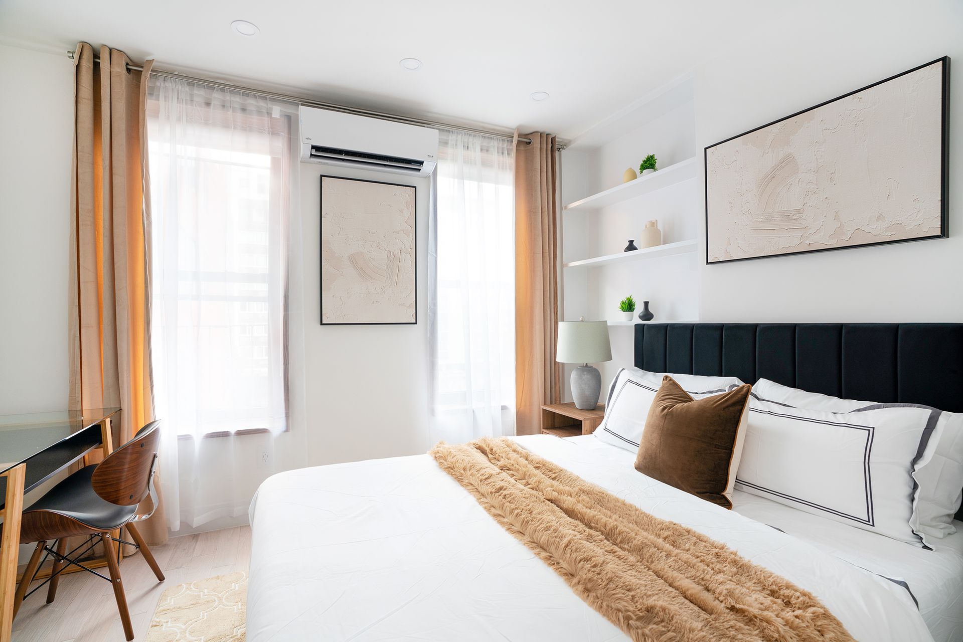 Bright one-bedroom apartment with a large bed, soft beige bedding, sheer curtains, and wall art. The apartment includes a washer and dryer and is located in Midtown West.