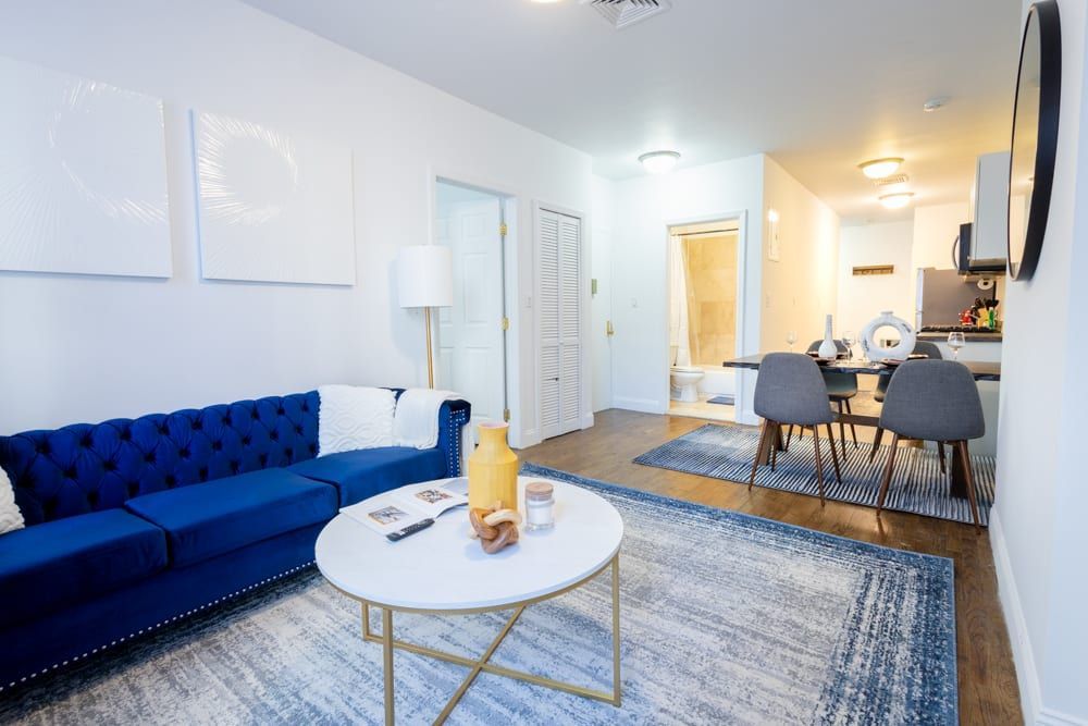 Spacious three-bedroom apartment with a blue sofa, round white coffee table, floor lamp, gray area rug, and dining area with gray chairs. The apartment has a washer and dryer and is located in the Upper East Side.