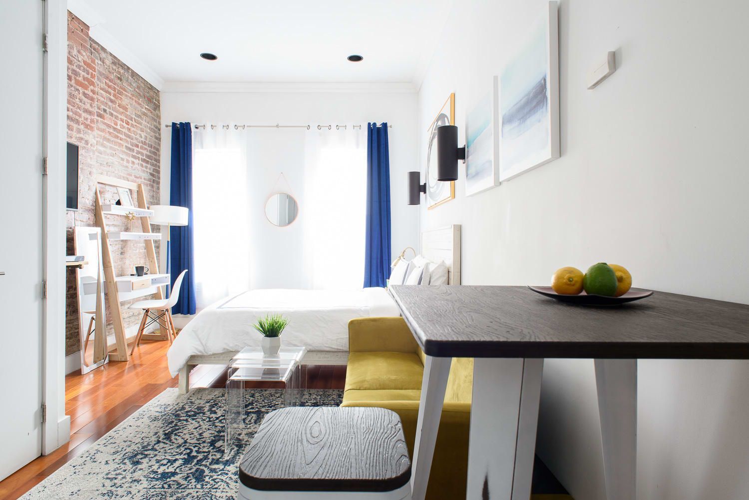 Modern studio apartment with bed, blue curtains, yellow seating, and a washer and dryer. Located in Gramercy/Murray Hill.