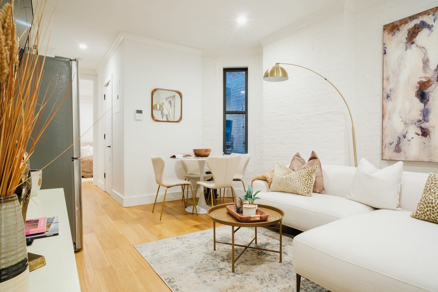 Bright two-bedroom apartment with a white sofa, wooden coffee table, round dining table with white chairs, and a gold floor lamp. The apartment is located in the Upper East Side.