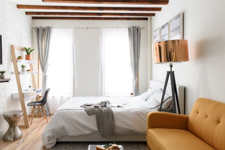 Studio apartment with a large bed, yellow armchair, grey curtains, and a washer and dryer. Located in Gramercy/Murray Hill.